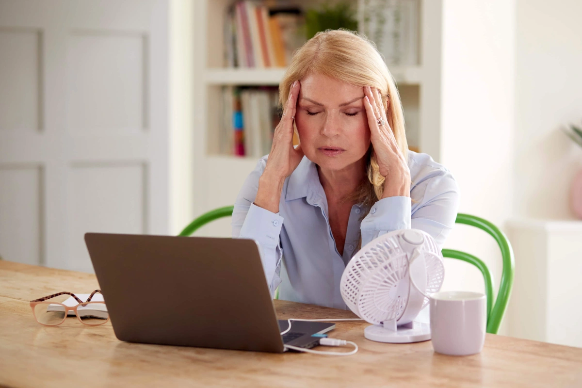 Woman experiencing hot flashes and menopause symptoms while working at a laptop, highlighting the need for Hormone imbalance treatment in Superior, CO